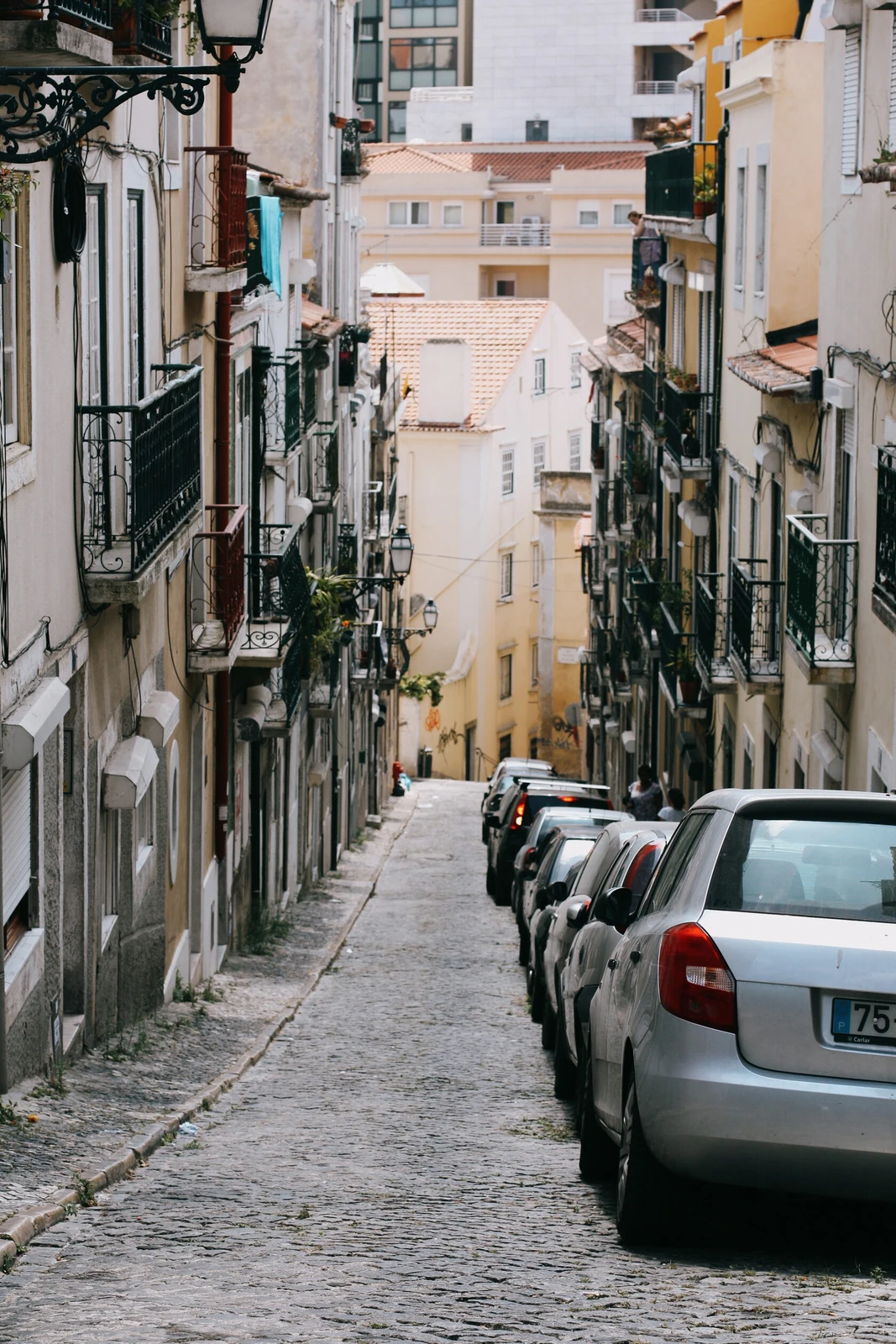 Vehicles parked in a narrow street with restricted sky visibility between buildings